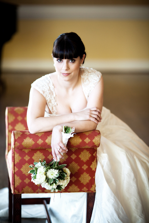 the beautiful bride with a retro hairstyle wearing an ivory ball gown style leaning on red and gold antique chair holding an ivory and green bouquet -  dress photo by North Carolina based wedding photographers Cunningham Photo Artists